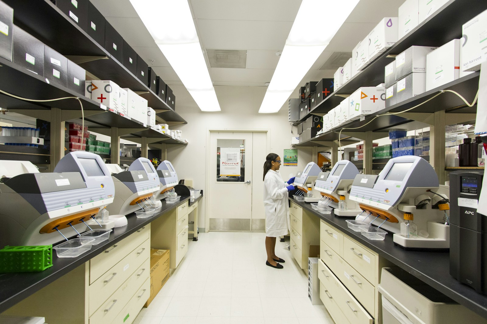 A laboratory technician standing beside genomic sequencing machines