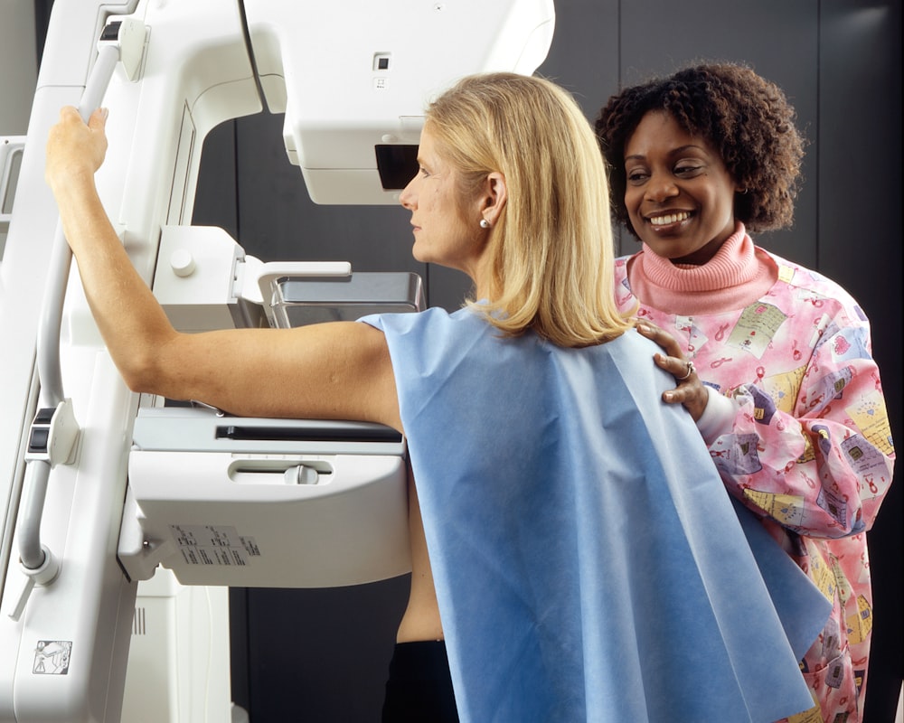 Donna sorridente in piedi vicino ad un'altra donna accanto alla macchina per mammografia