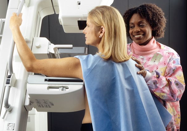 smiling woman standing near another woman beside mammogram machine