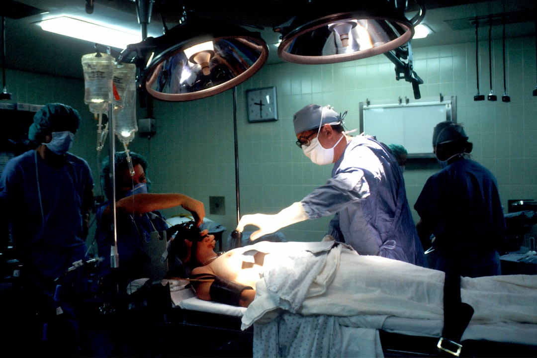 Biopsy. A Caucasian woman patient is being prepared for surgery. Her left breast is visible and anesthesia is being administered. The male physician has his hand extended and is examining the patient. Several operative attendants are also visible. A surgical biopsy is being performed to determine exact nature of solid tumor. Creator: Linda Bartlett