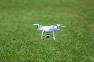 A white quadcopter drone is hovering closely above a lush, green grassy field.