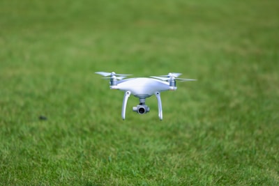 A white quadcopter drone is hovering closely above a lush, green grassy field.