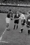 A group of diverse football players shaking hands on a sunny urban pitch