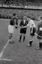 A handshake between a football agent and a player on a sunlit stadium pitch.