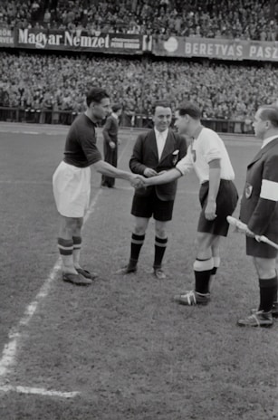 A handshake between a football agent and a player on a sunlit stadium pitch.