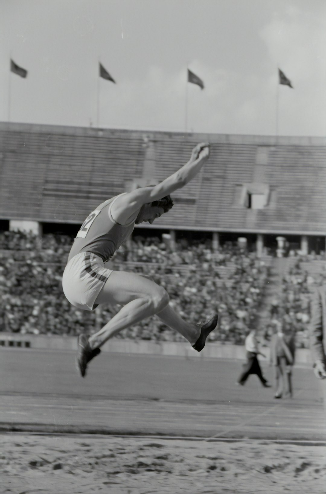  grayscale photography of man doing high jump surrounded with people watching record player