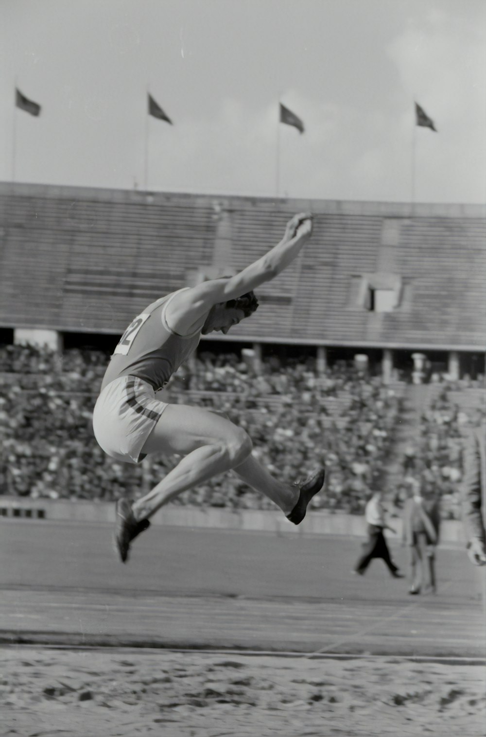 grayscale photography of man doing high jump surrounded with people watching