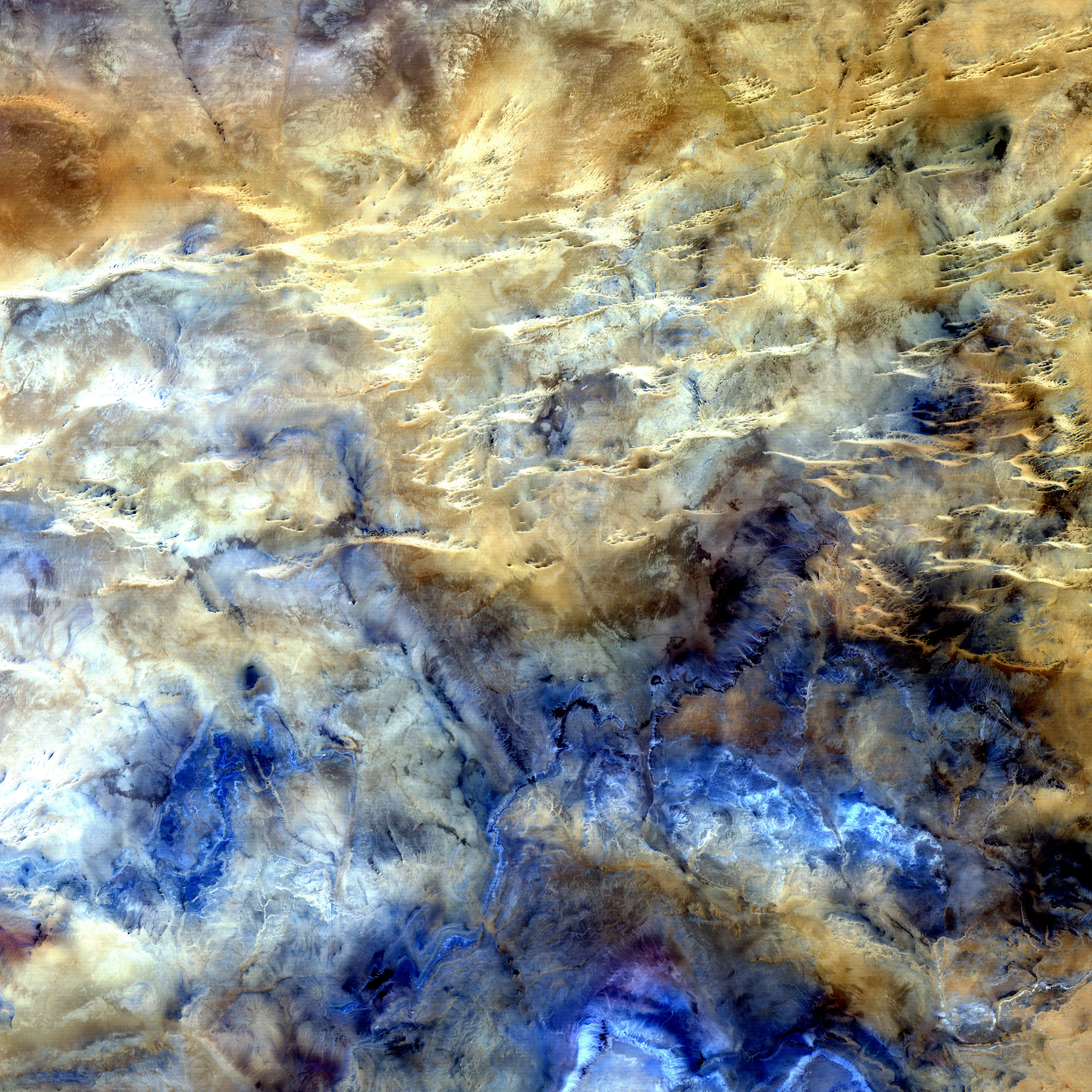 A study in shades of blue and brown is actually one of the harshest landscapes on Earth. This glimpse of Africa's Sahara Desert, located near where the borders of Mali, Niger, and Algeria converge, is truly a no man's land, a world of sand and rock without roads or settlements. The horizontal lines across the top half of the image are intrusions of igneous rock, where magma poked up to the surface from deep underground.