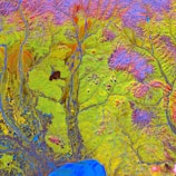 A vibrant satellite image displaying intricate patterns of rivers and water bodies across a landscape dominated by green and red hues. The intricate network of blue streams is interspersed with red-tipped ridges, set against a predominantly green and yellow terrain.