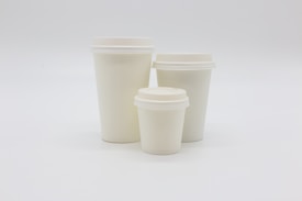 Three white paper cups of varying sizes are placed against a plain white background. The cups are arranged with the smallest in front and the largest at the back.
