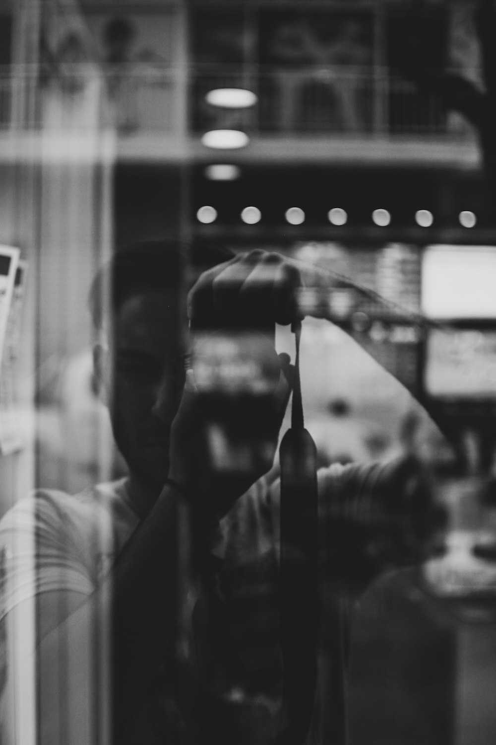 grayscale photography of man taking photo reflecting on glass wall