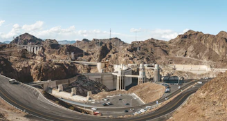 A group of engineers examining blueprints beside a large earth dam under construction on a sunny day.