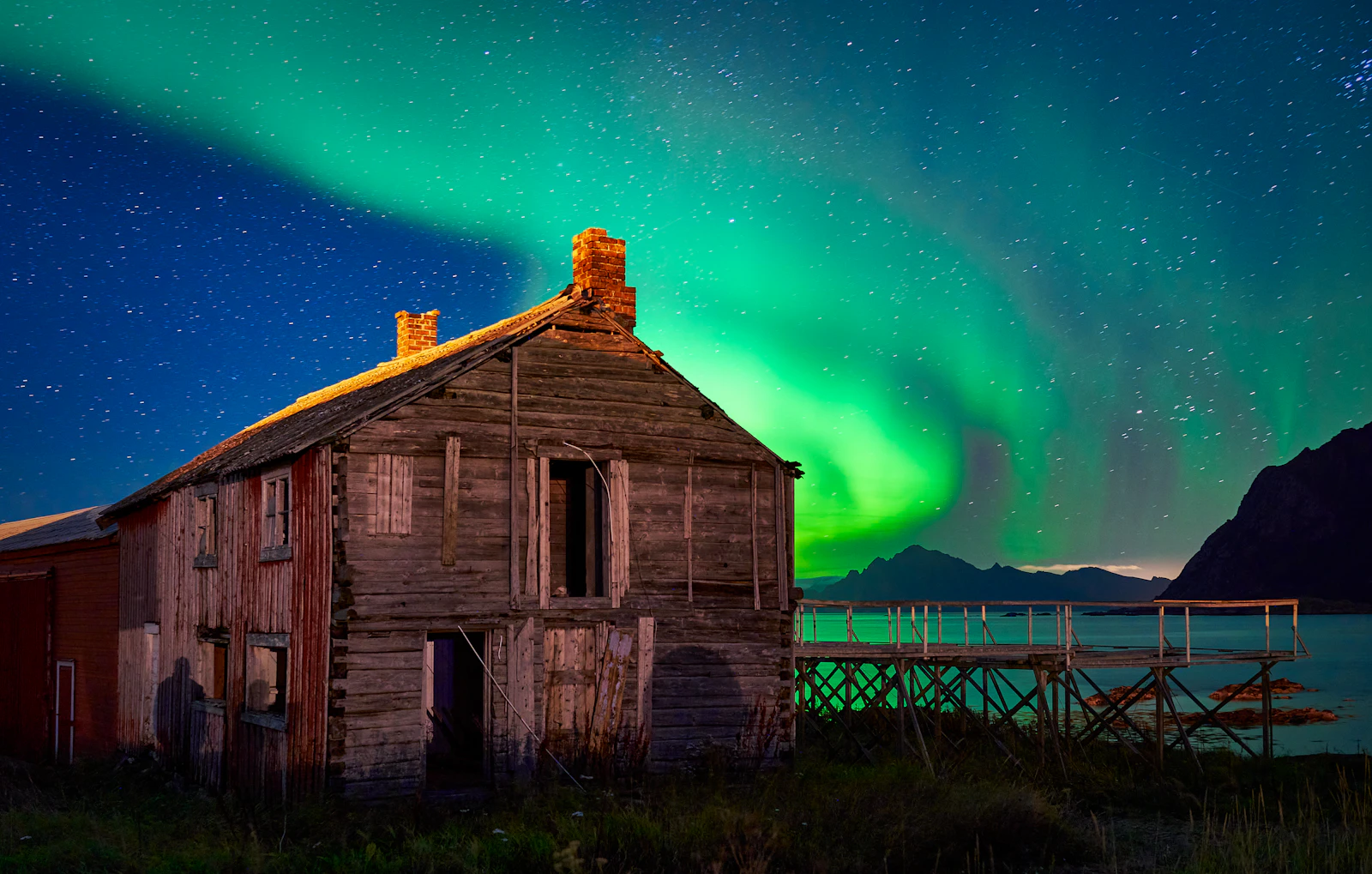 Aurora borealis over a grey wooden boathouse at night in Bø i Vesterålen