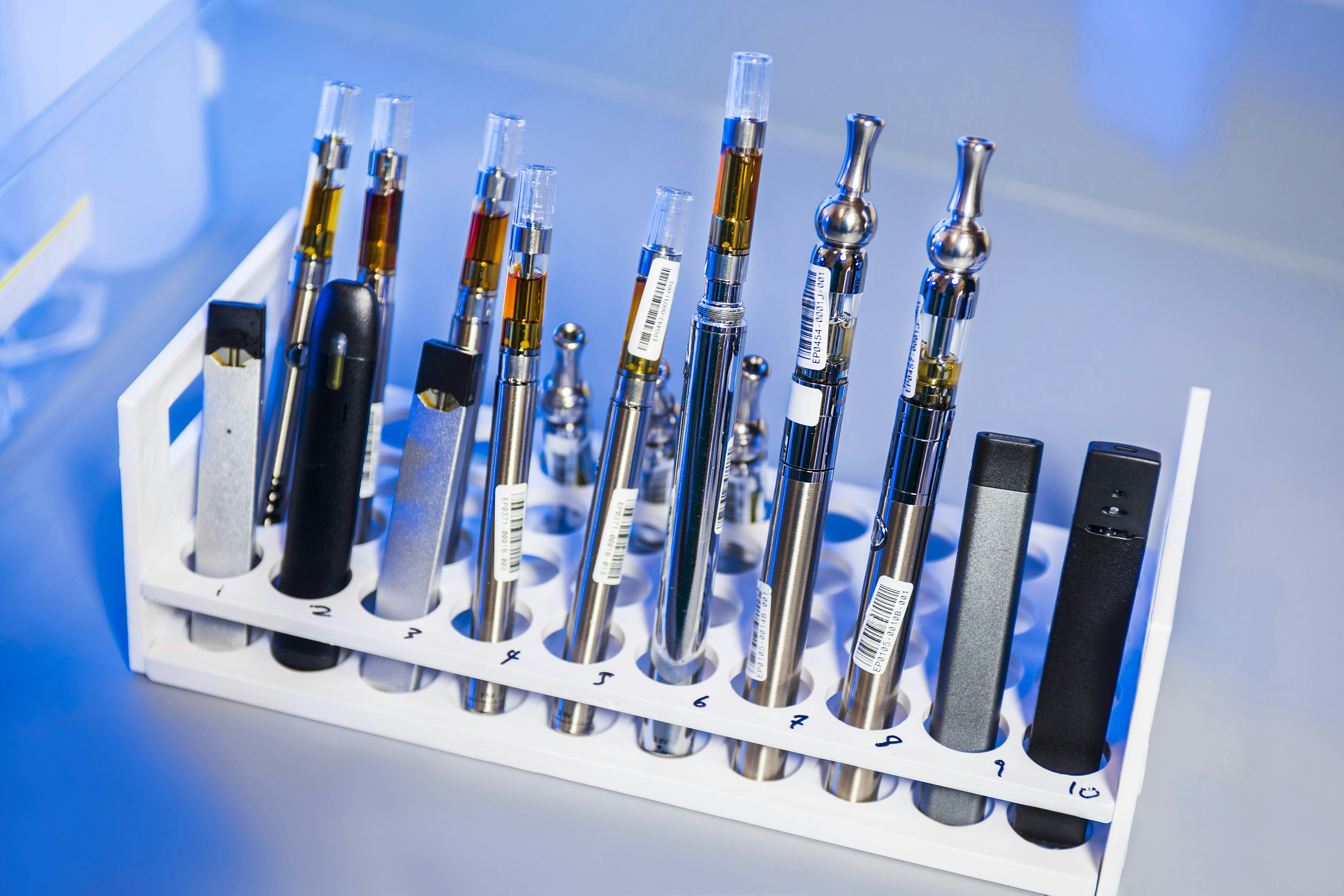 This image depicted a test tube rack that had been stocked with examples of various electronic cigarettes, referred to as e-cigarettes, or e-cigs, and vaping pens. These items would undergo testing in...