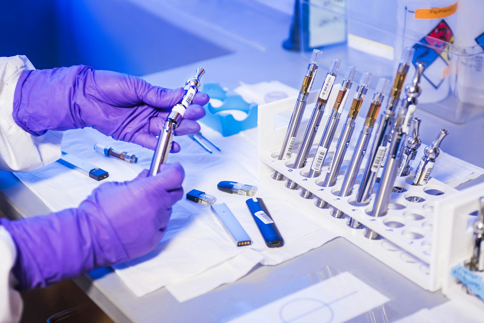 Here you see the gloved hands of a Centers for Disease Control and Prevention (CDC) laboratory technician working with electronic cigarettes, referred to as e-cigarettes, or e-cigs, and vaping pens, while inside a laboratory environment.