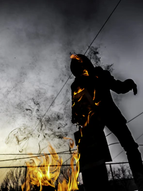 A mysterious character silhouetted against a dark, fiery background.