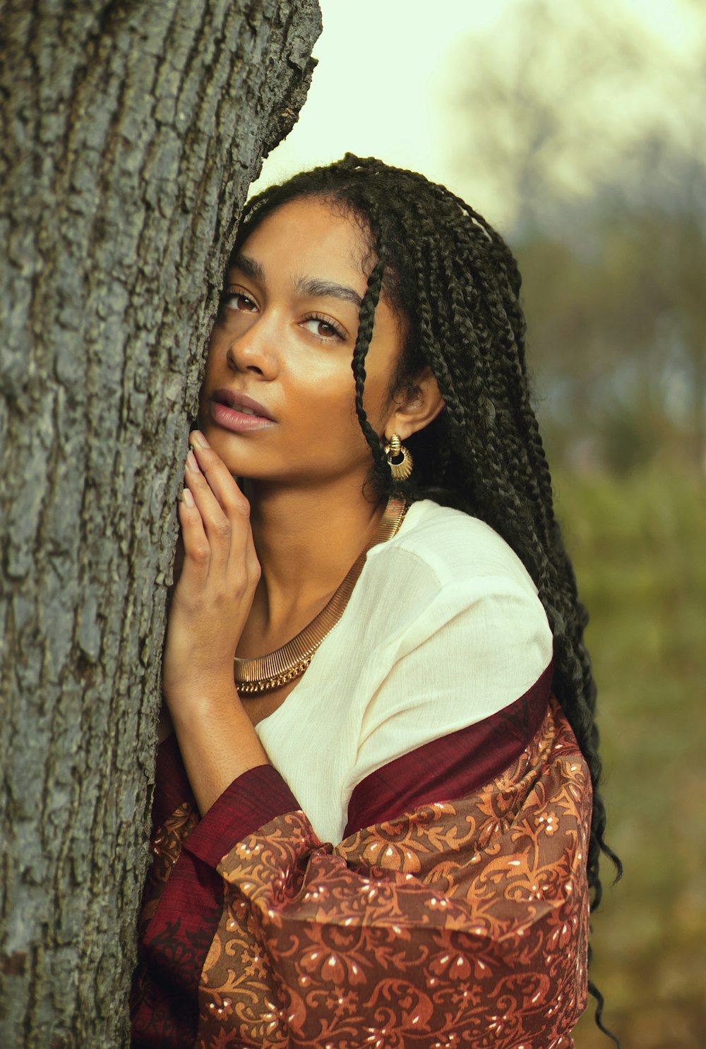 woman in white top leaning on tree