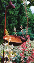 A decorative bird bath featuring a rustic metal basin atop a wooden stand, surrounded by blooming flowers.