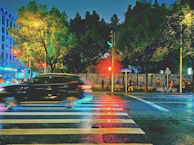 A city street scene with a compact car waiting at a crosswalk under bright city lights.