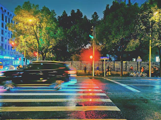 A city street scene with a compact car waiting at a crosswalk under bright city lights.