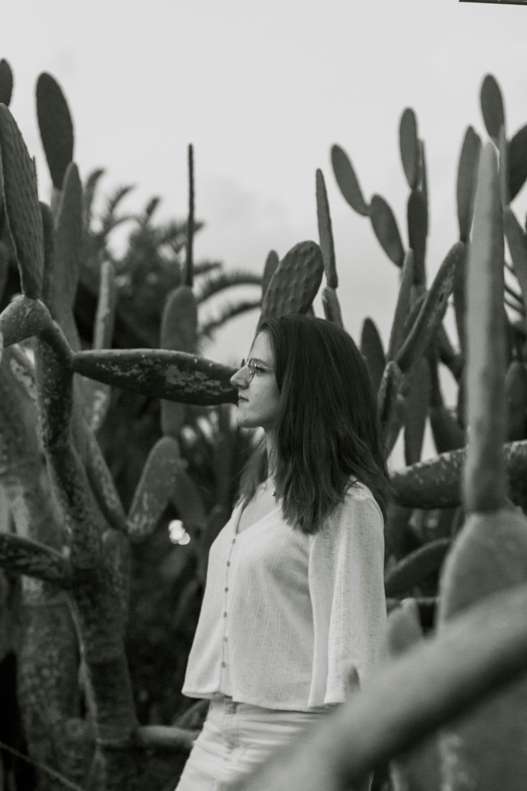 grayscale photo of woman standing near cactus plant