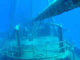 Underwater perspective of a hull with barnacles and marine life clinging to its surface.