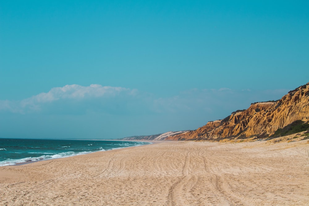 a sandy beach next to the ocean under a blue sky