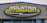 A large, rectangular business sign reads 'Mountain Motorsports' in bold letters. The text 'MOUNTAIN' is white, while 'MOTORSPORTS' is yellow, both set against a dark background. Above the text, there is an outline of mountain peaks in yellow.