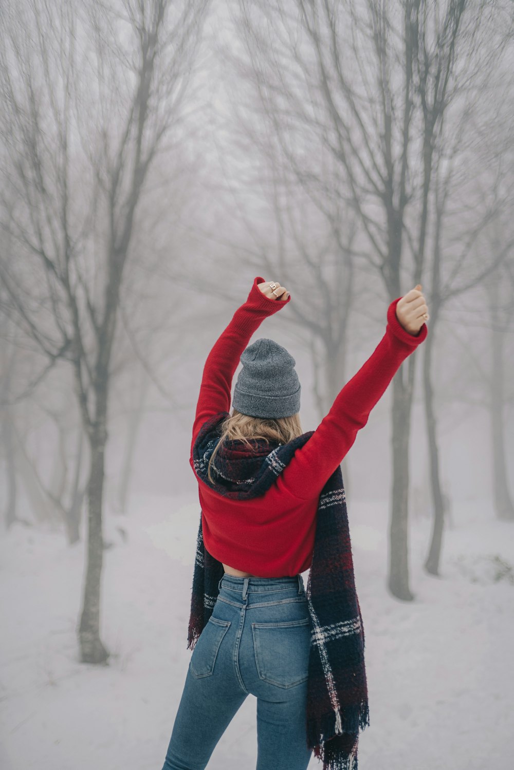 femme levant ses deux mains face aux arbres nus couverts de neige
