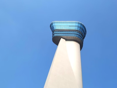 A modern control tower, with a sleek design featuring a glass-paneled section at the top, rises against a clear blue sky.
