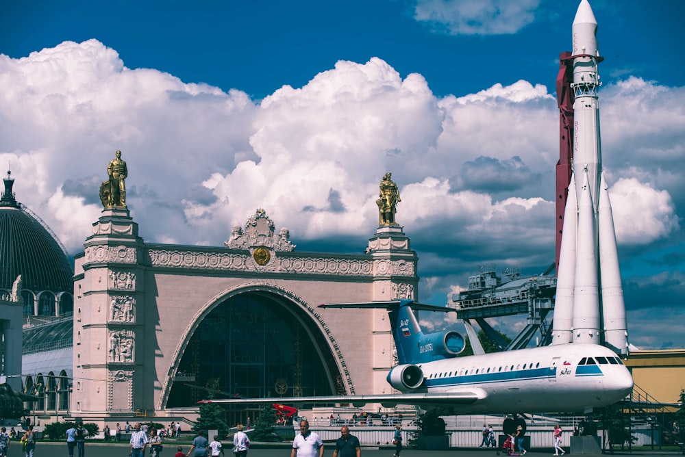 pessoas andando perto de branco e cinza edifício histórico e aeroporto sob o céu branco e azul