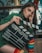 A person with long hair is holding a film clapperboard labeled 'Universal Studios'. They are wearing a green sweater and have rainbow-striped socks. The background features shelves and some decor items.