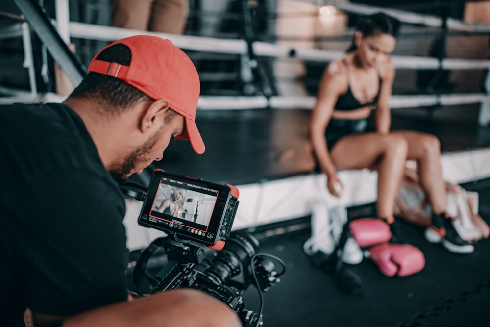 man taking video of woman wearing black bra and black shorts while sitting near pink boxing gloves