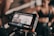 A digital camera screen displays a close-up of a person in athletic wear, possibly recording a fitness video. The person appears to be smiling and is in a well-lit space with a ring-like setting visible in the background.