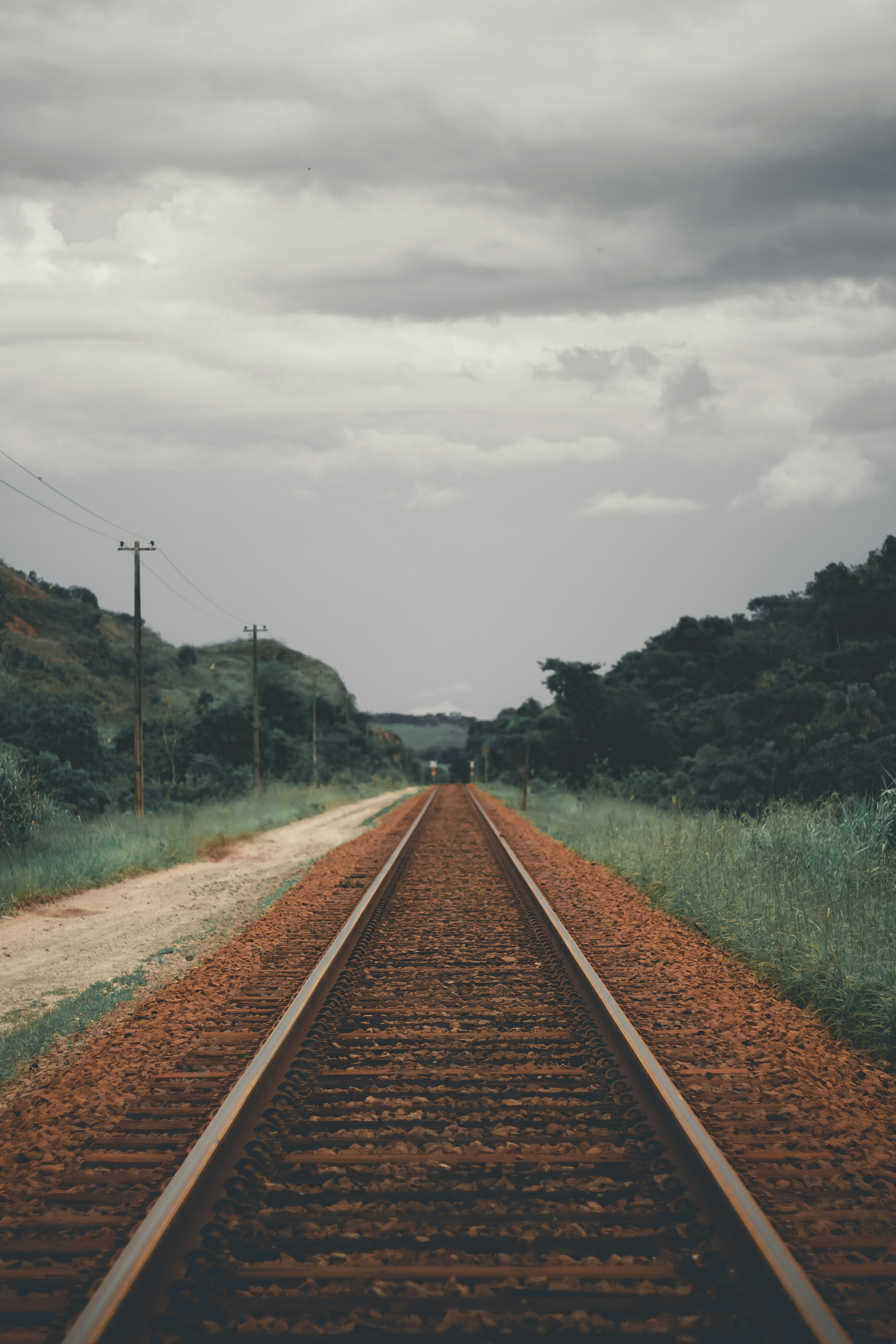 brown train railway near green field surrounded with green trees under white and gray sky