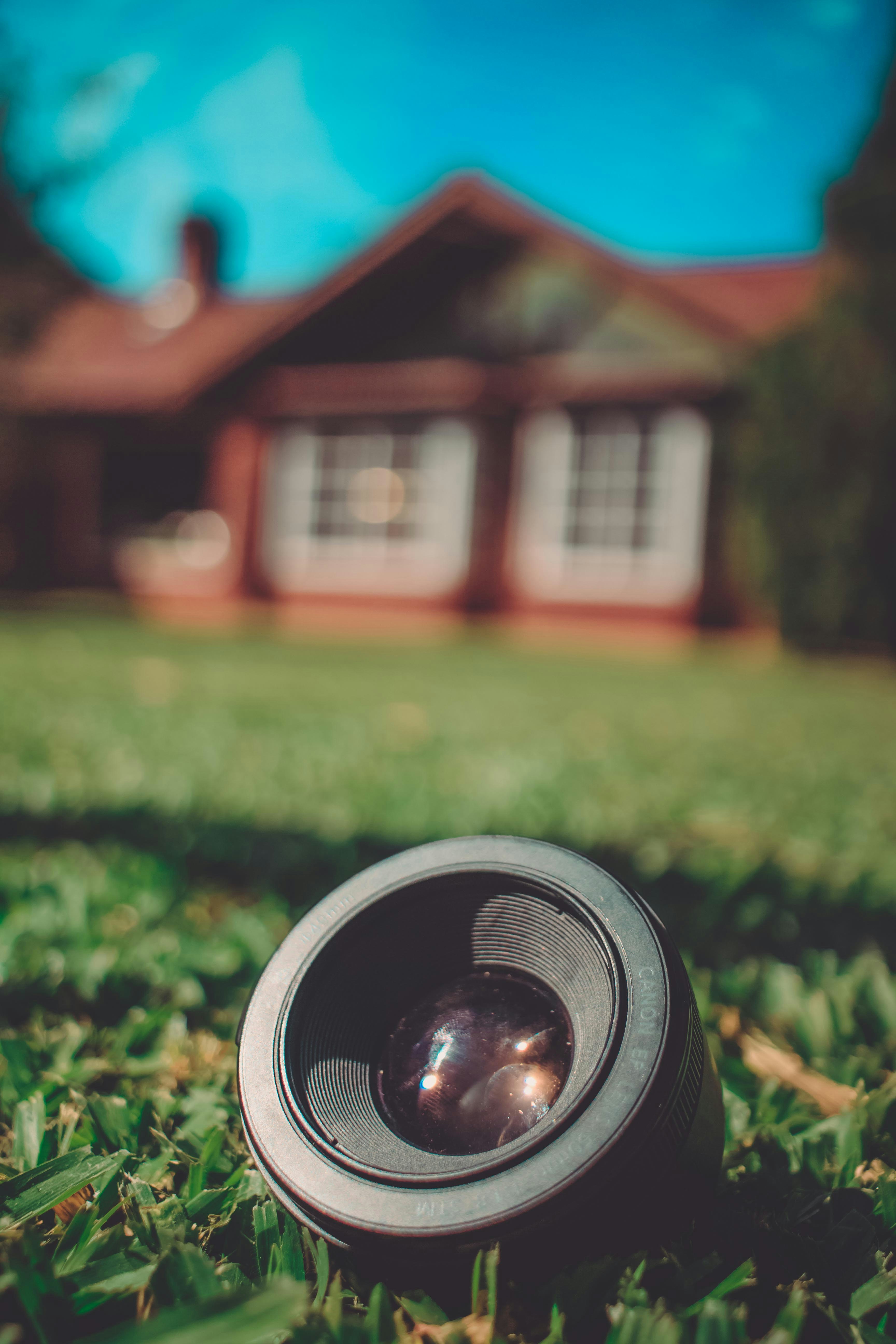 black camera lens on green field viewing brown house
