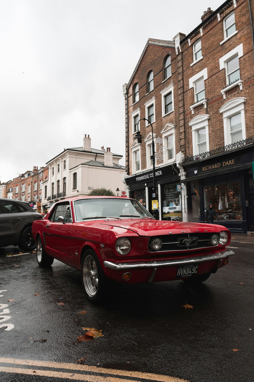 classic parked red Ford Mustang coupe near buildings and cars during day