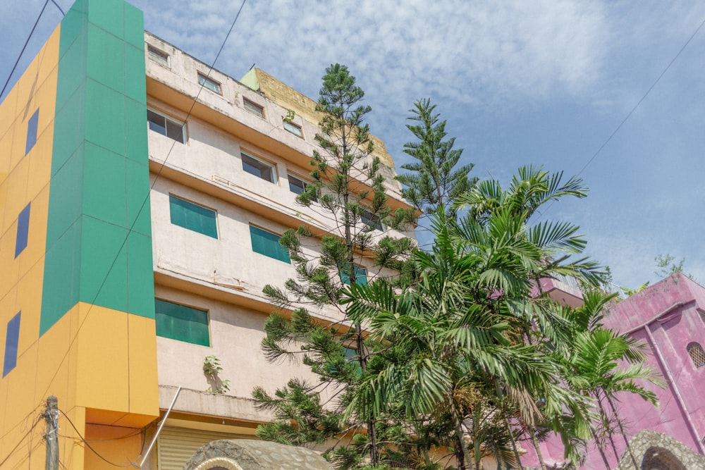 white, green, and yellow high-rise building near green trees under white and blue sky