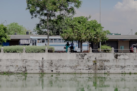 two people standing near white and blue bus beside buildings surrounded with green trees under white and blue sky in Colombo Sri Lanka