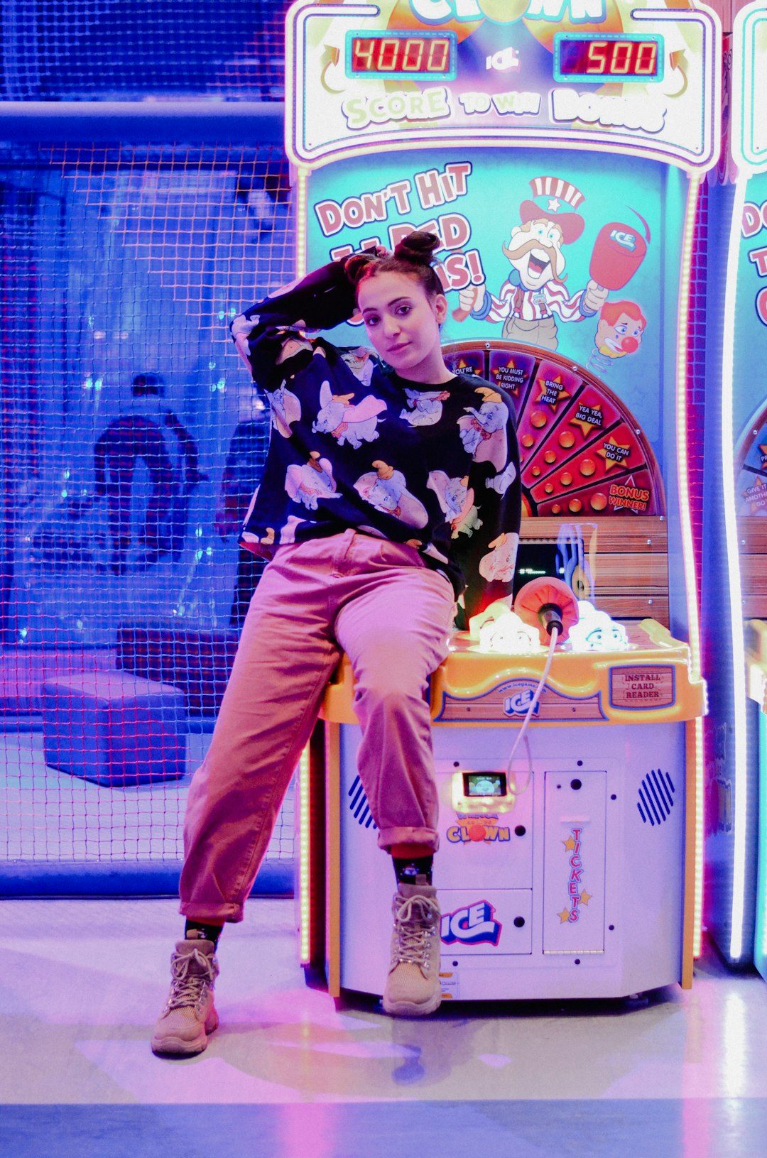woman wearing black and multicolored floral crew-neck sweatshirt sitting on multicolored arcade machine