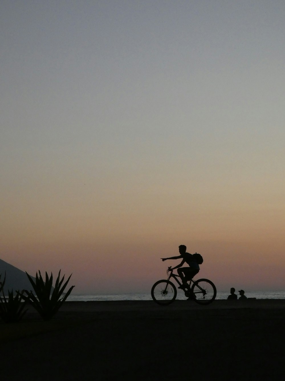 homme faisant du vélo près de deux personnes à la plage pendant l’heure dorée