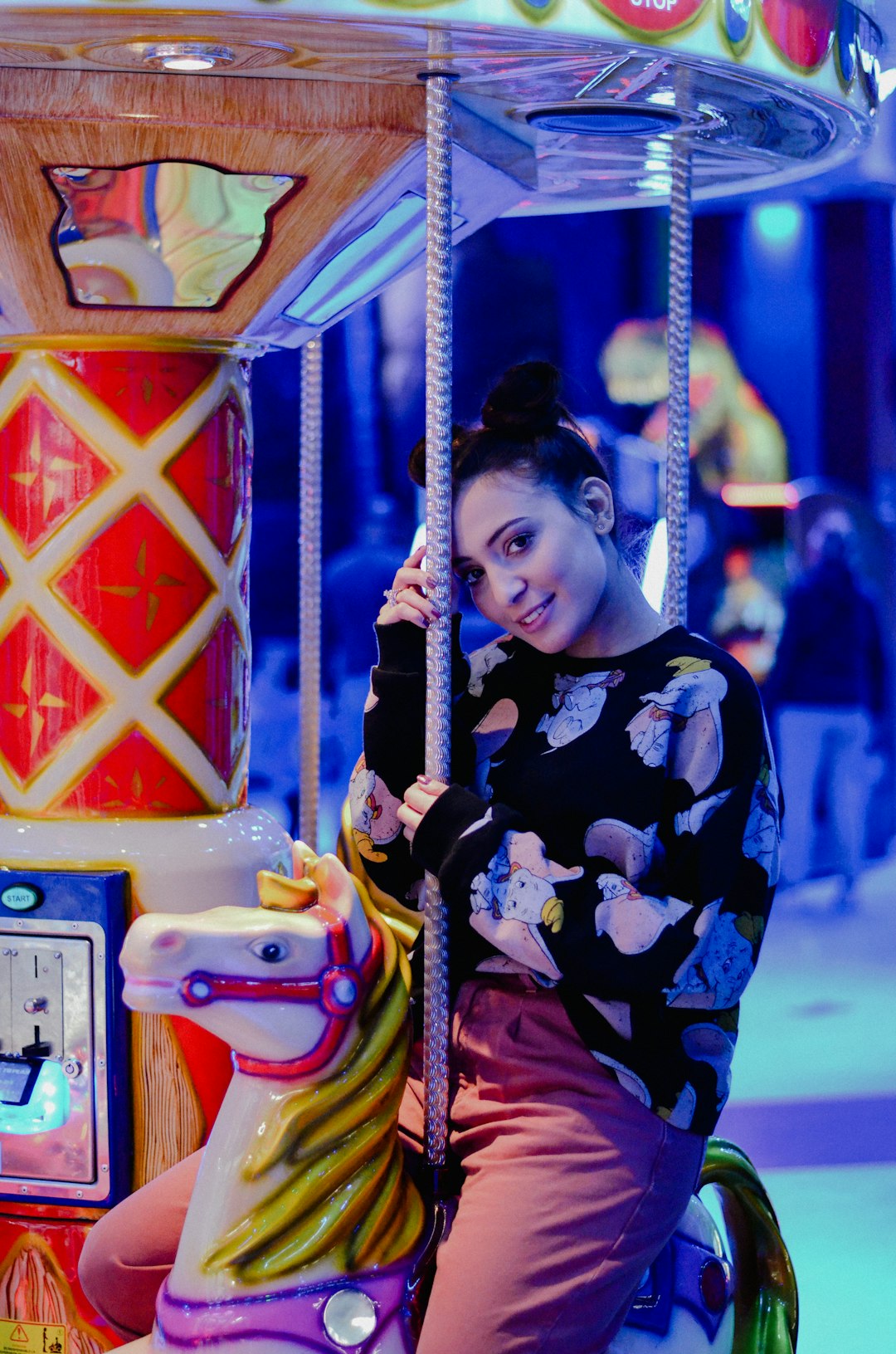 smiling woman wearing black and multicolored crew-neck sweatshirt sitting on carousel ride