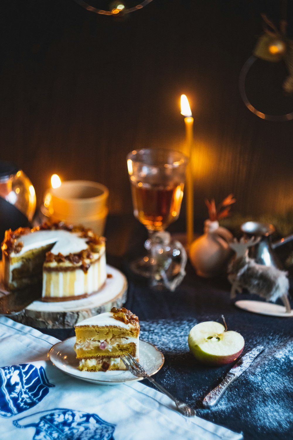 lighted candlestick near glass of white wine, sliced cake, apple fruit, and knife