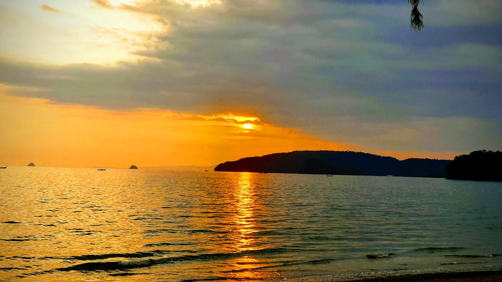 body of water viewing mountain under orange and blue sky