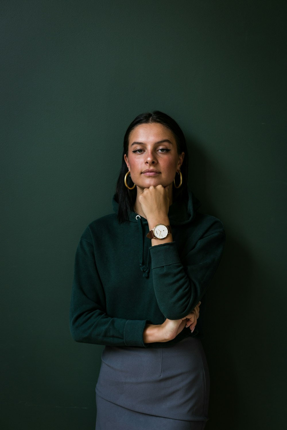 woman wearing green collared sweater and gold-colored earrings standing while putting left hand on her chin