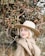 smiling woman wearing brown coat and beige hat standing near flowering tree
