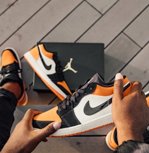 person sitting and holding white, orange, and black Air Jordan 1 low-top sneaker