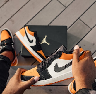 person sitting and holding white, orange, and black Air Jordan 1 low-top sneaker