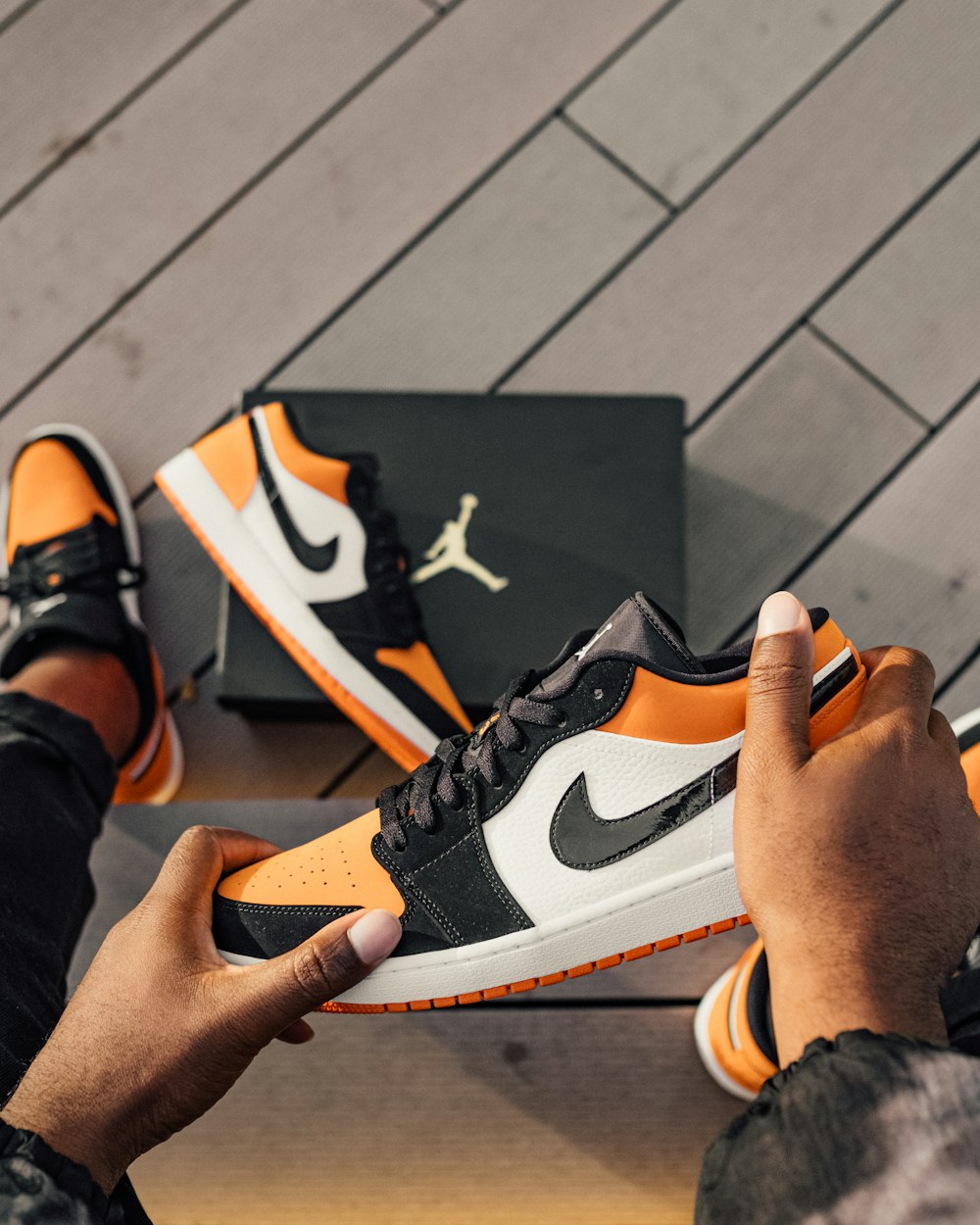 Person, die sitzt und weißen, orangefarbenen und schwarzen Air Jordan 1 Low-Top-Sneaker hält