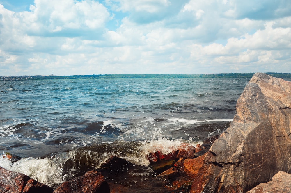 brown rock formations near body of water under white and blue sky